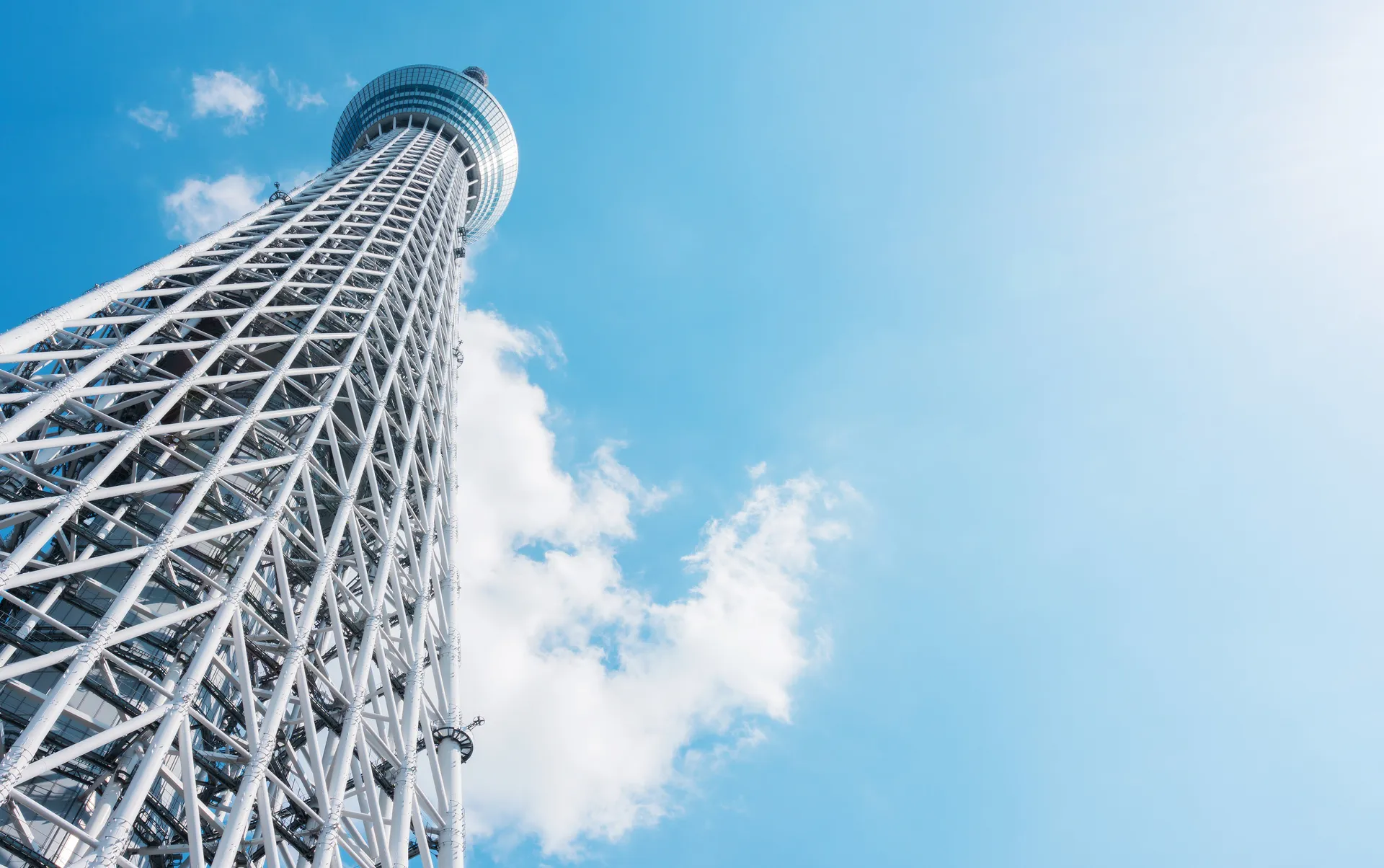 青空に向かって高くそびえ立つ、東京スカイツリーの白い鉄骨構造を見上げた写真。