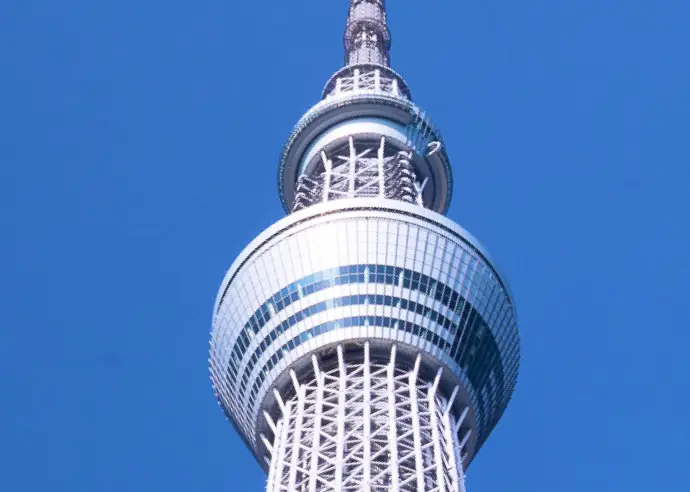 青空を背景に、天望デッキを含む東京スカイツリー上部の鉄骨構造を近距離から見上げた写真。
