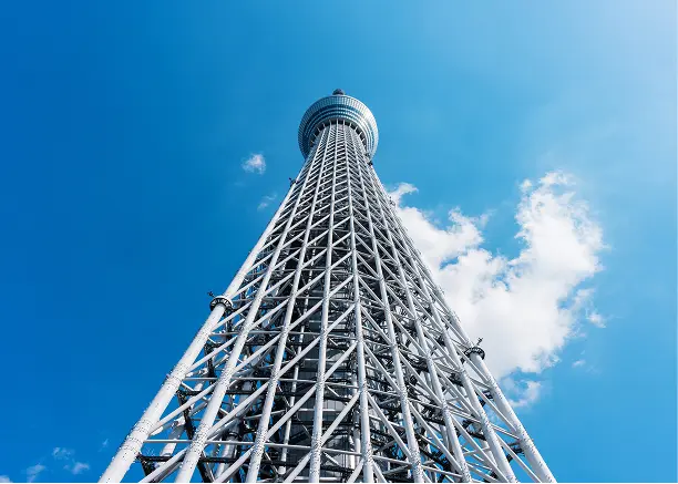 晴れ渡る青空に向かってそびえ立つ、東京スカイツリーの白い鉄骨構造を下から見上げた様子