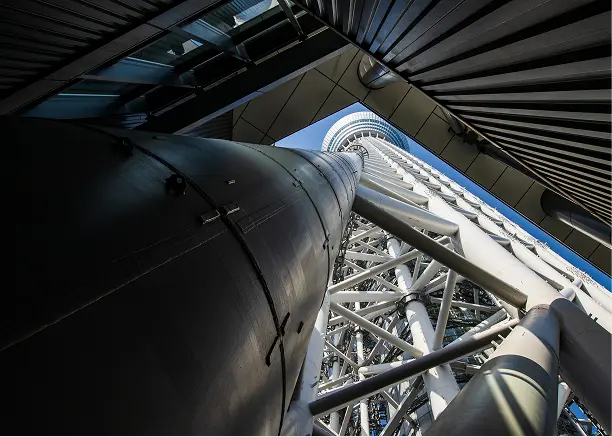 塔の内部から見上げた、中央を貫く巨大なグレーの円柱（心柱）と、それを囲むように組まれた白い鉄骨構造