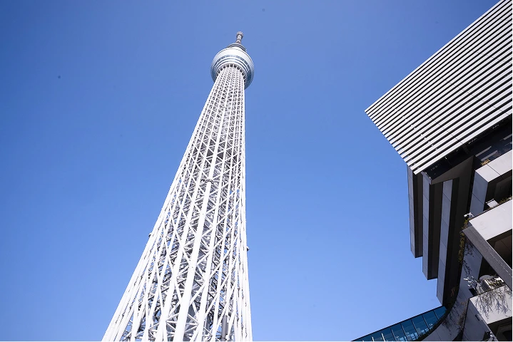 屋外スペースから遠くに東京スカイツリーを望み、作業着姿の人物が測定している様子