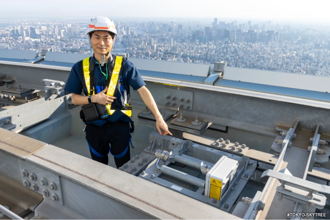 東京スカイツリーの屋上で安全装備を着用し、産業用設備を点検するエンジニア