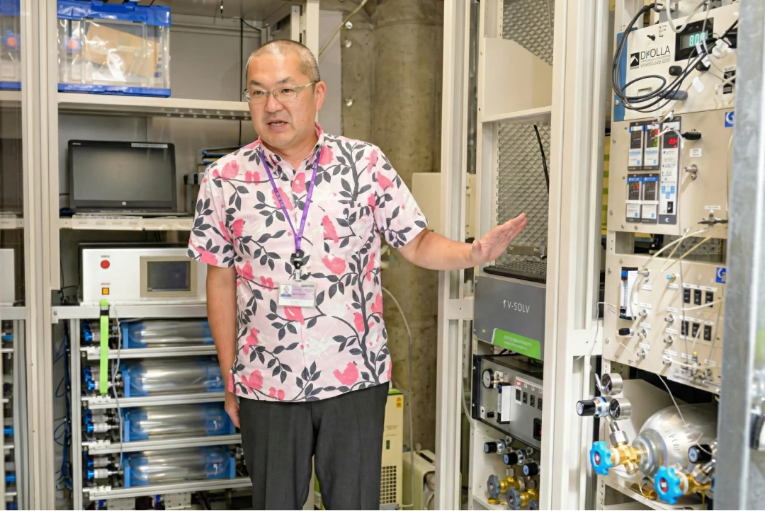 観測室内でフラスコサンプリング装置や分析機器の仕組みを説明する専門家