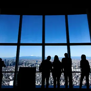 展望フロアの大きな窓から東京の街を眺める人影