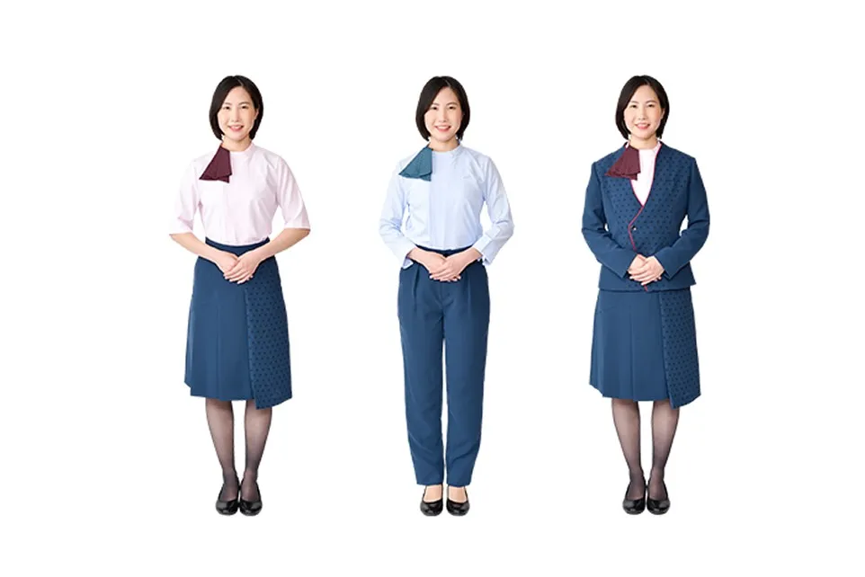 Three different Uniform for female Staff at the Fast Skytree Ticket Counter . From left to right: a light pink short-sleeved blouse and navy skirt, a light blue long-sleeved blouse and navy pants, and a navy jacket and skirt. The jacket on the far right has a red line (piping) around the collar, as described in the explanation. The skirt has an asymmetrical design with origami-like pleats on the left side.