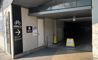 西駐輪場の入り口付近。建物の壁面に自転車のマークと右矢印が描かれた黒い看板があり、奥へ進む通路を示している。