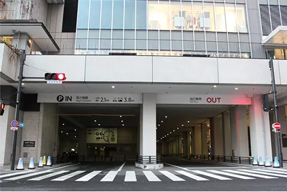 建物の1F部分にある立体駐車場の出入口。左側が『IN 入口』、右側が『OUT 出口』と表示されており、手前には横断歩道があります。