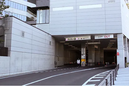 地下駐車場の東側出入口。手前から奥に向かって下りスロープが伸びており、左側が入口、右側が出口に分かれています。それぞれのゲート上部には『IN 入口』『OUT 出口』の看板があります。