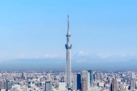 青空の下、東京の街並みの中心にそびえ立つ東京スカイツリーの全景。
