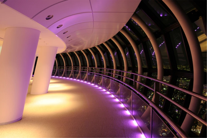 紫色のライティングが足元を彩る夜の天望回廊と、窓の外に広がる都心の夜景