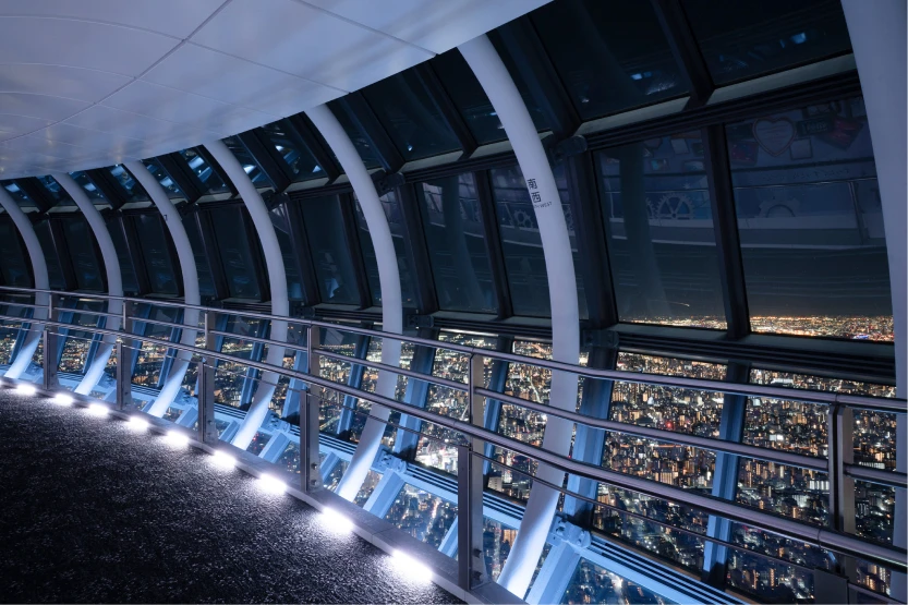 白い光に照らされた夜の天望回廊の通路と、ガラス越しに見える広大な夜景