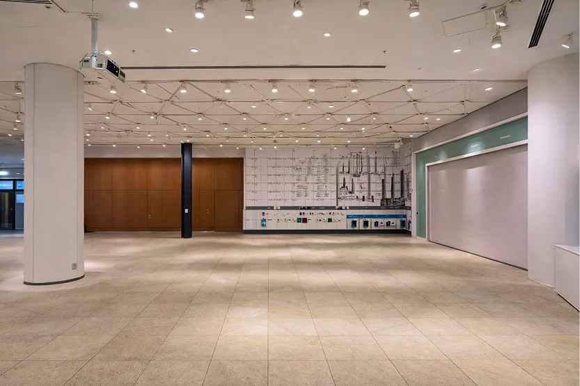 ベージュの石畳風の床が広がるガランとした室内。奥の壁にはグラフィックデザインが施され、木目調のドアが見える。