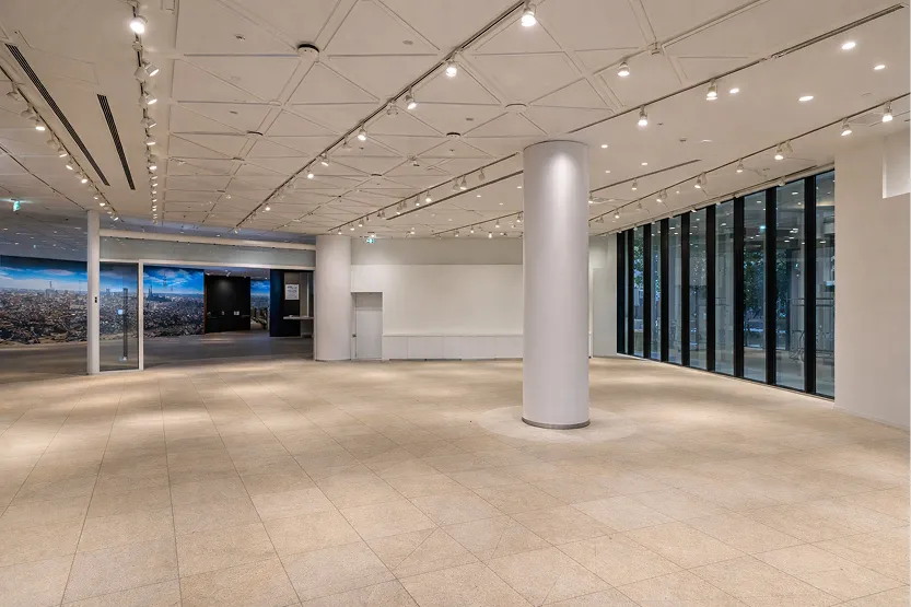 大きな柱がある開放的なホール。右側には外の景色が見える全面ガラス窓があり、天井にはスポットライトが張り巡らされている。