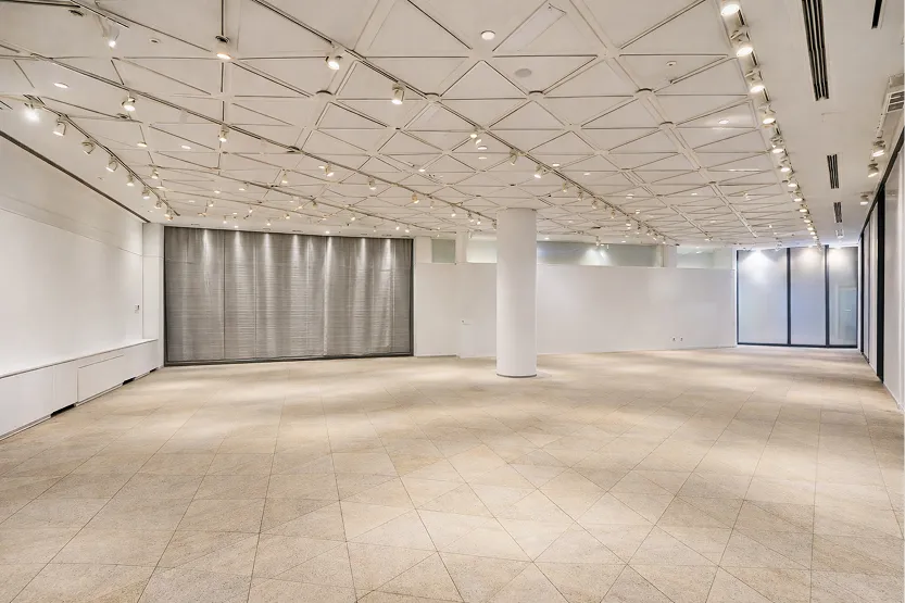 天井の格子状の照明レールが特徴的な、何もないイベントフロア。奥にはグレーのカーテンや仕切りが見える。