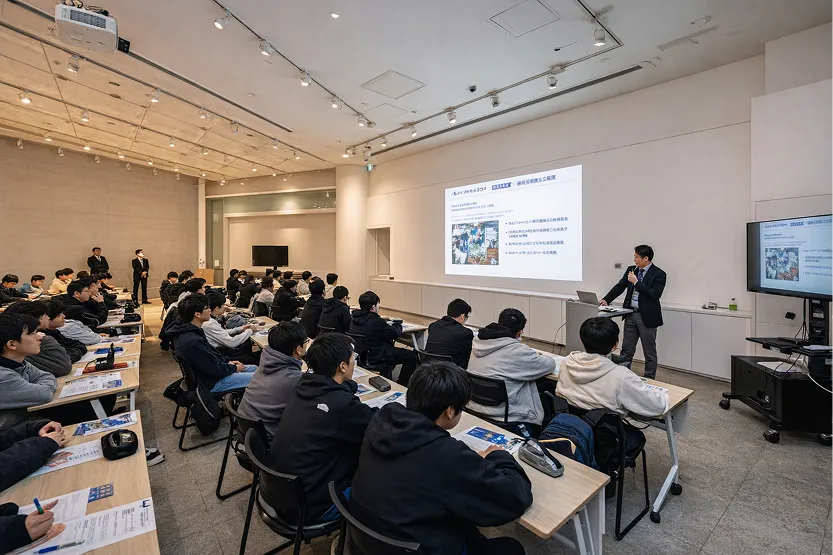 多くの参加者が着席し、前方のスクリーンを見つめているセミナーの様子。右側では講師が立ち、スライドを使って説明している。