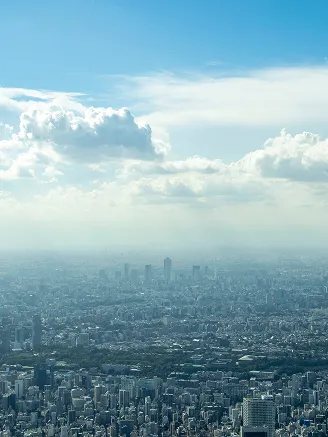 澄み渡る青空と白い雲の下、地平線まで広がる東京の広大な街並みを高い視点から捉えたパノラマ写真。