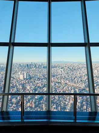 展望台の大きな垂直の窓枠から見下ろす、昼間のビル群の俯瞰風景。