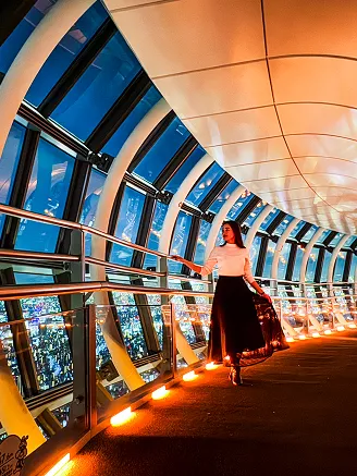 夜の展望回廊を歩く女性。窓の外には広大な東京の夜景が点滅している。