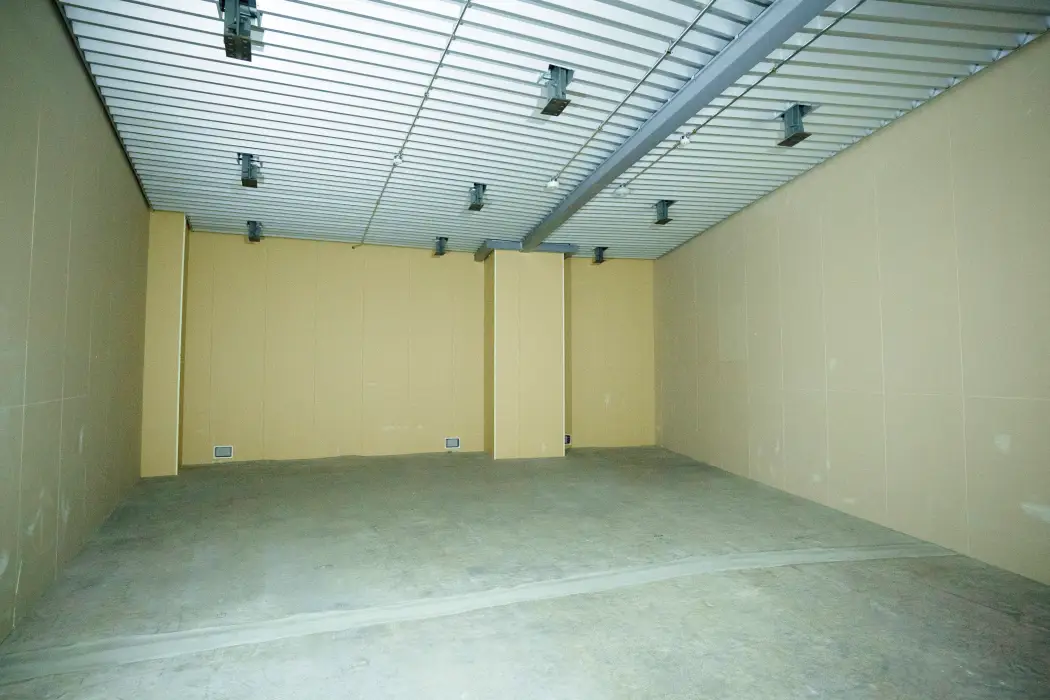 広い空間に薄黄色い壁とグレーの床、天井に等間隔の照明と梁がある屋内機器室