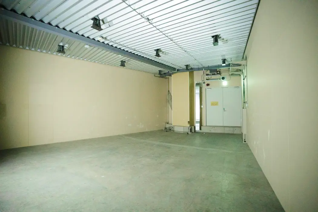 屋内機器室の別角度。奥に白い扉と配管、壁面に設置された電気設備が見える様子