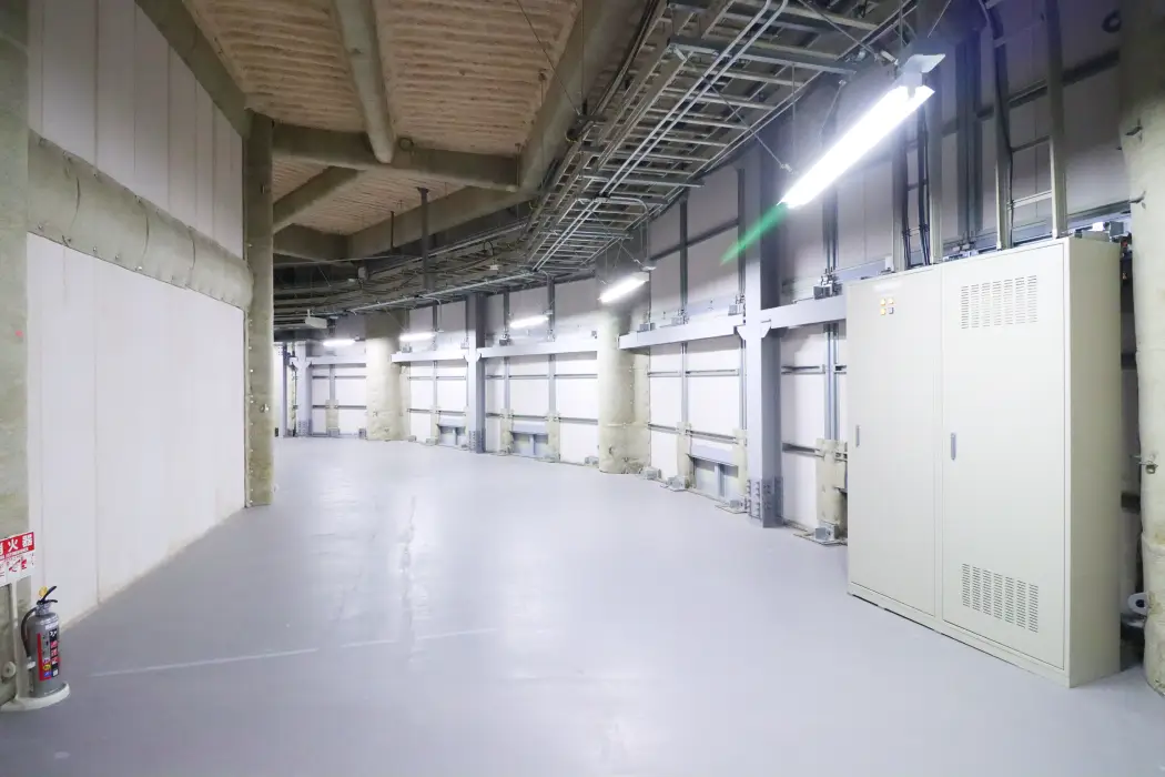 屋内の鉄骨柱の間に設置された、ベージュ色の金属製配電盤と計器類