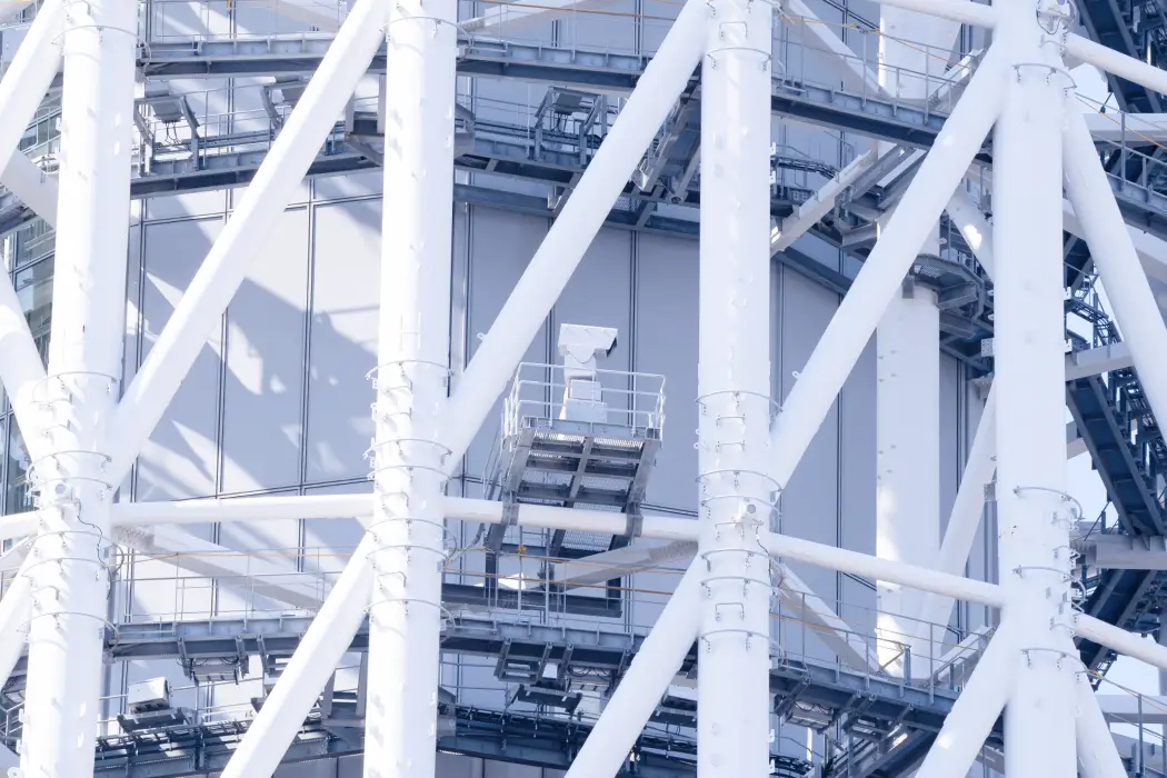 複雑に組まれた白い鉄骨トラスの間に設置された、銀色の高感度防災監視カメラ