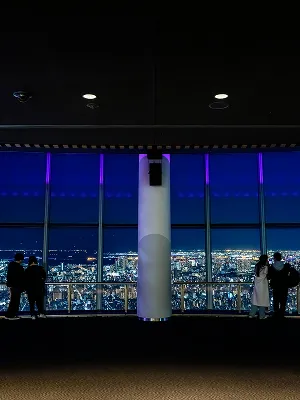 夜の展望フロアから見た、ライトアップされた東京都内の景色。ガラス越しに、東京の夜を象徴する暖色系の光が浮かび上がっている。