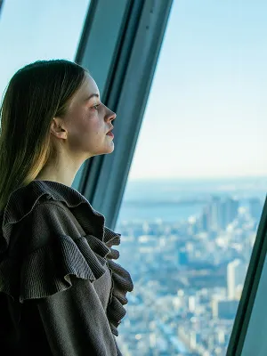 展望台の大きな窓の前に立ち、遠くを見つめる女性の横顔。窓の外には広大な昼間の都市風景が広がっている。