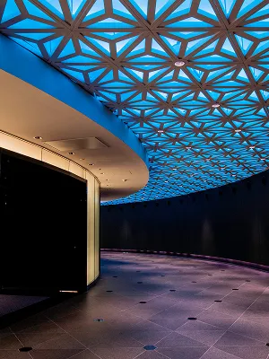 特徴的な網目状の天井デザインが施された、夜の展望回廊。青白い照明が未来的な雰囲気を演出し、外には夜景が見える。