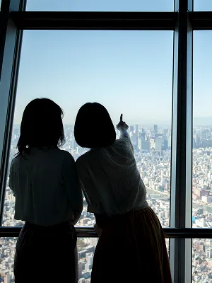 ガラス越しに広大な景色を見つめる、二人の女性のシルエット。遠くの地平線までよく見える