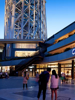 スカイツリーの足元にある東京ソラマチ。日が暮れ始めた時間帯、ライトアップされた建物と、そこを歩く人々のリラックスした様子。