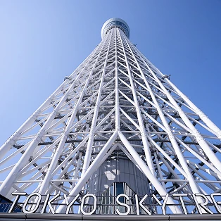 足元から真上に見上げた、幾何学的に組まれた東京スカイツリーの白い鉄骨と青空。