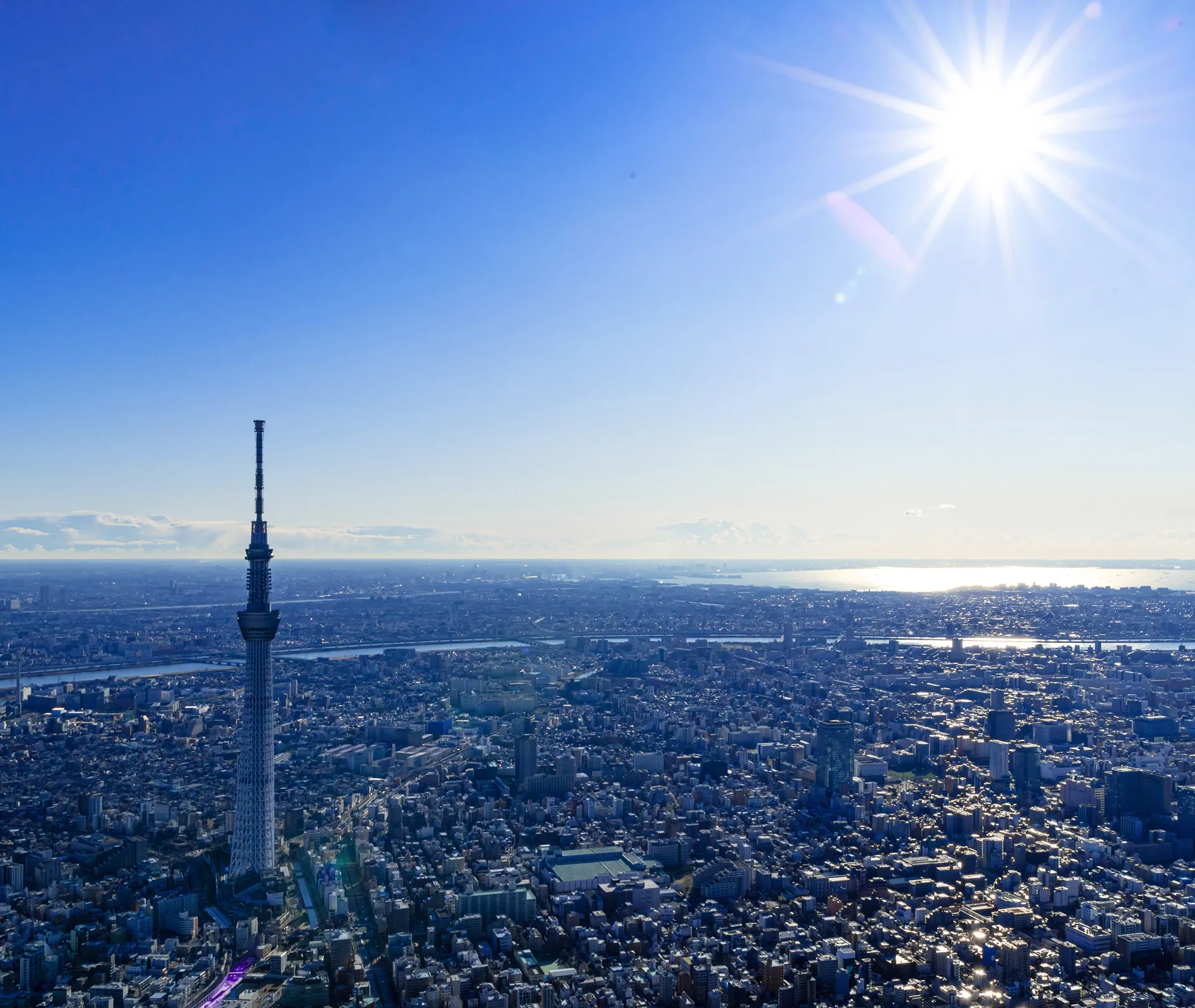 太陽が眩しく輝く、昼間の天望デッキからの眺望。遥か遠くの地平線まで見渡せる都市の景色と、澄み渡る青い空のコントラスト。