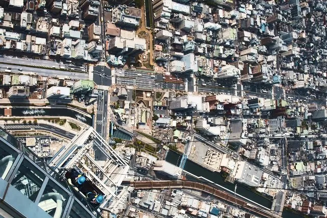 東京スカイツリー天望回廊の窓の外、日本一高い場所で清掃作業を行うゴンドラと、足元に広がる街の俯瞰景。