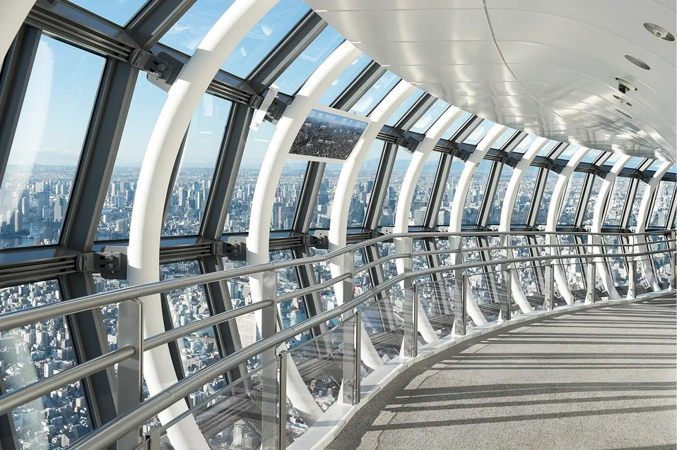 緩やかな曲線を描く、白く明るい東京スカイツリーの天望回廊。足元まで広がる大きな窓からは、地平線まで続く広大な東京の街並みを一望できる。