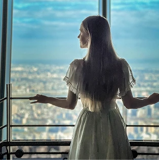 展望台の窓際に立ち、外の景色を眺める女性の後ろ姿