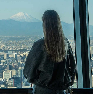 展望台の窓から遠くの富士山と街並みを眺める2人の女性の後ろ姿