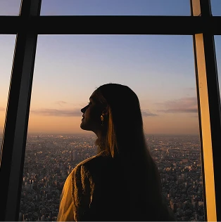 夕日を背景に展望台の窓際に立つ女性の横顔のシルエット