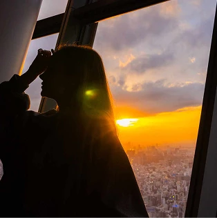 窓の外の夕日を眺める女性のシルエット