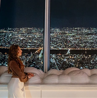 白い雲のようなベンチの横から夜景を眺める女性