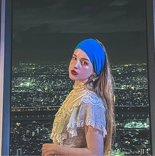 青いヘアバンドを着け、夜景を背景に窓辺に立つ女性