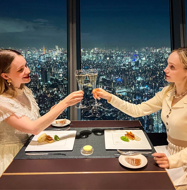 夜景が見えるレストランの窓側の席で乾杯する2人の女性