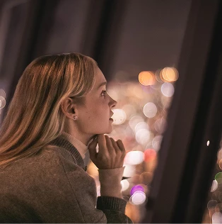 夜景の光のボケを背景にして外を見つめる女性の横顔