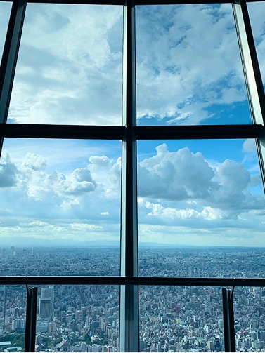 展望台の大きな窓から青空と白い雲、街並みを眺める様子