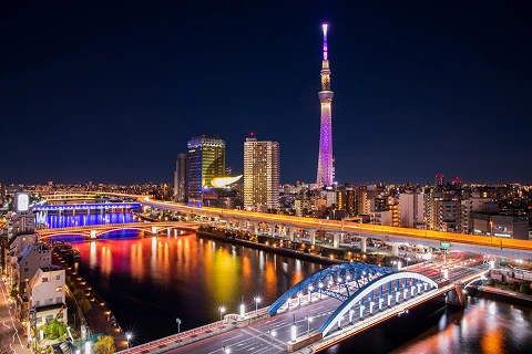 夜の川に架かるライトアップされたアーチ橋と奥に見える東京スカイツリー