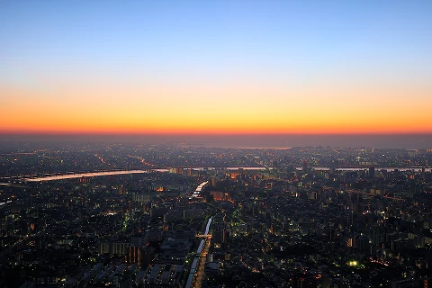 夕焼けのグラデーションに染まる空と、川が流れる東京の街並みの空撮