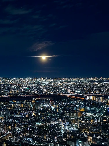 薄い雲の切れ間から輝く月と、眼下に広がる光の海のような東京の夜景