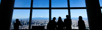 展望台の窓から富士山と街並みを眺める人々のシルエット