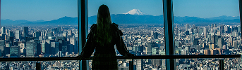 展望台の窓から街並みと富士山を眺める女性の後ろ姿