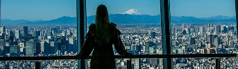 展望台の窓から街並みと富士山を眺める女性の後ろ姿